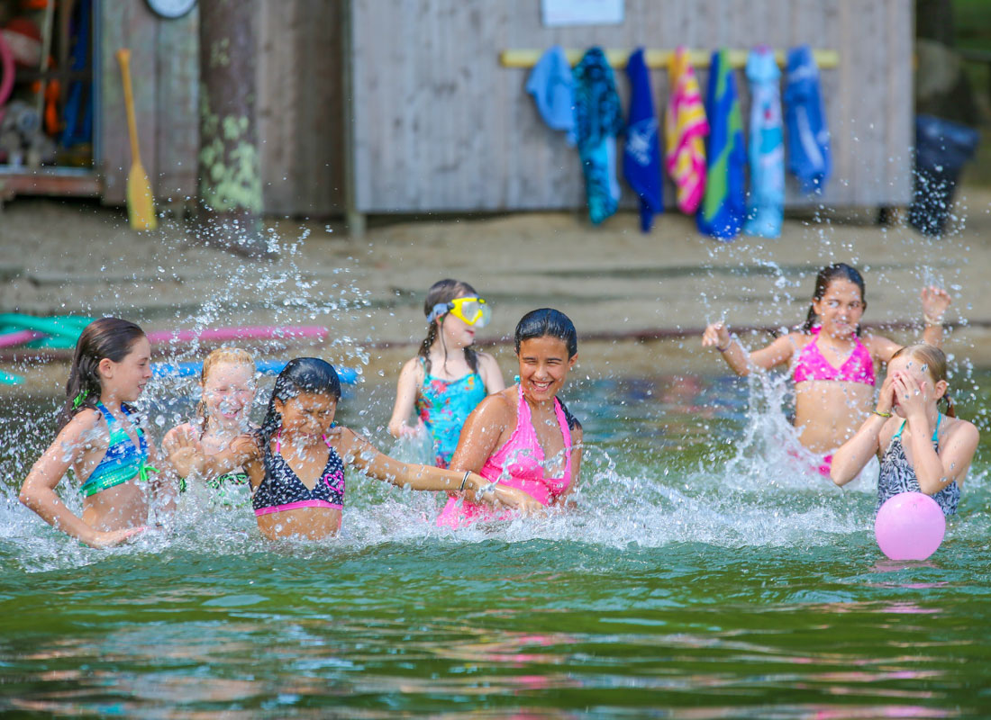 girls at summer camp splashing in water at lake