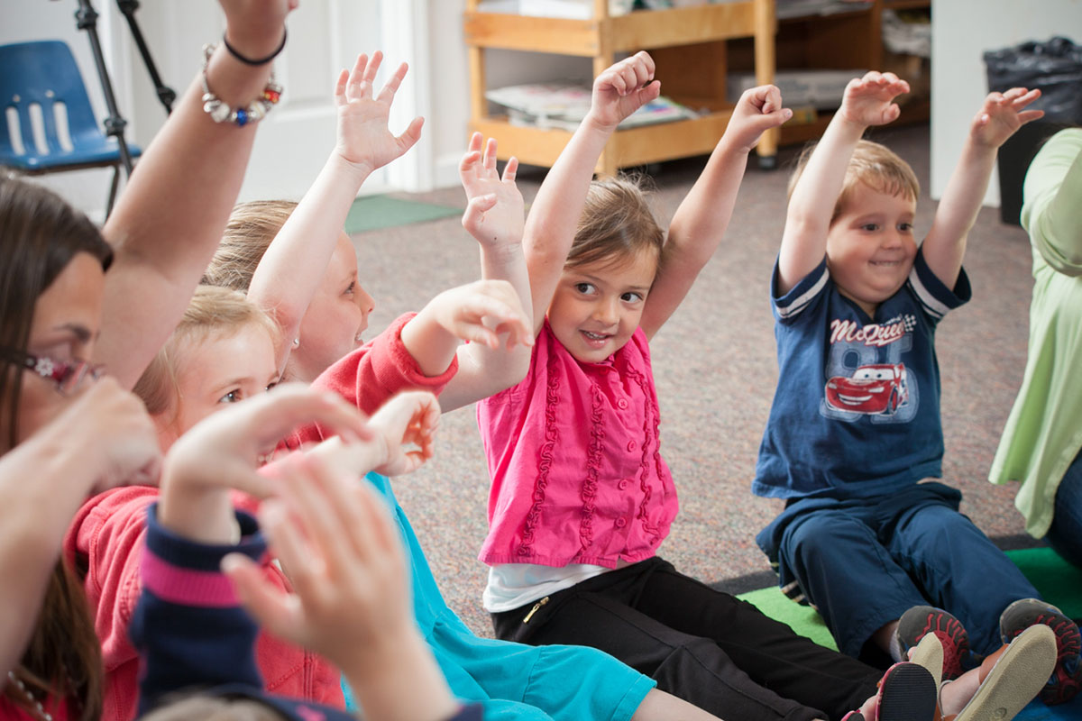 young students raising hands in circle at school