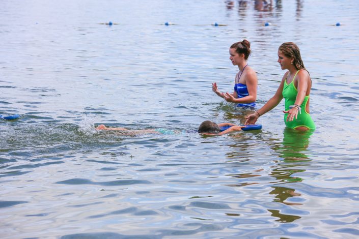 two female camp staff members teaching girl how to swim